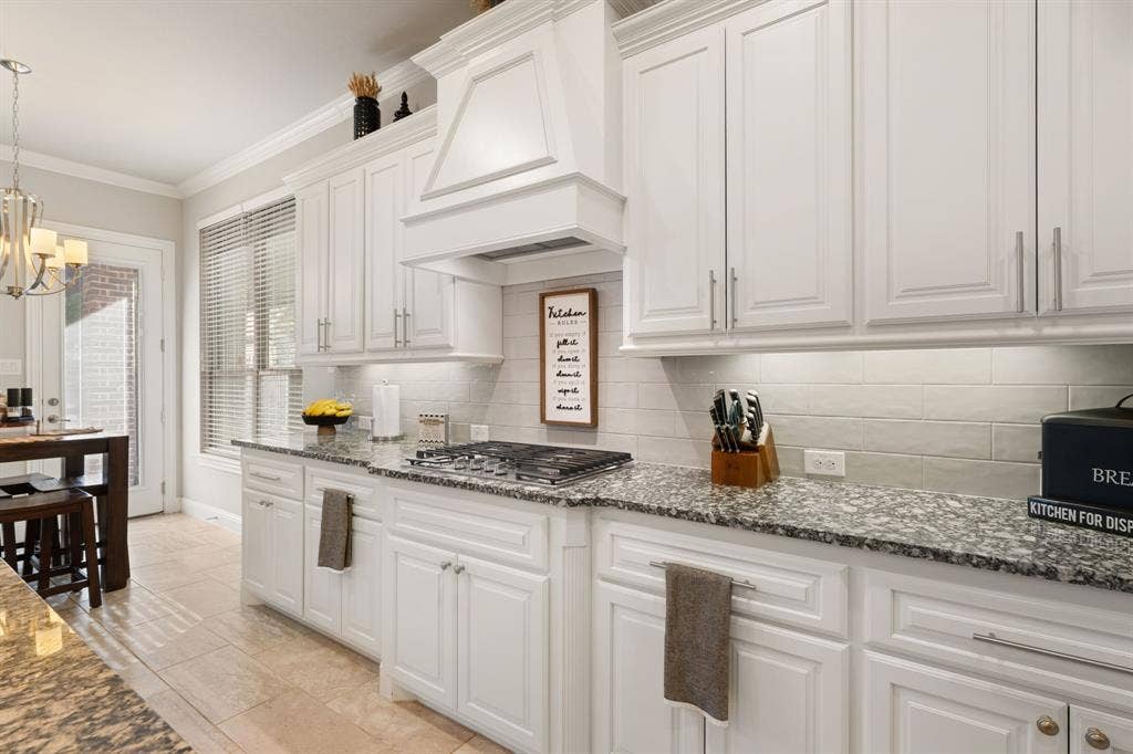 White shaker-style cabinetry, a built-in range hood, light-toned backsplash tiling, and stone countertops