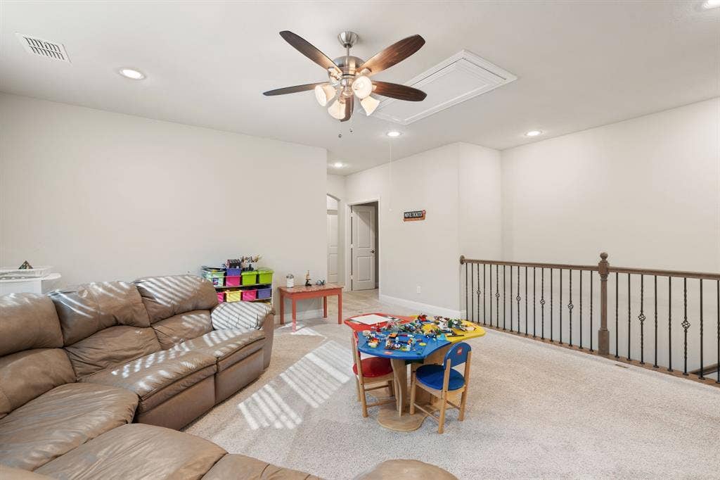 Carpeted loft area featuring a ceiling fan with integrated lighting, recessed lighting, and a wrought iron and wood baluster railing