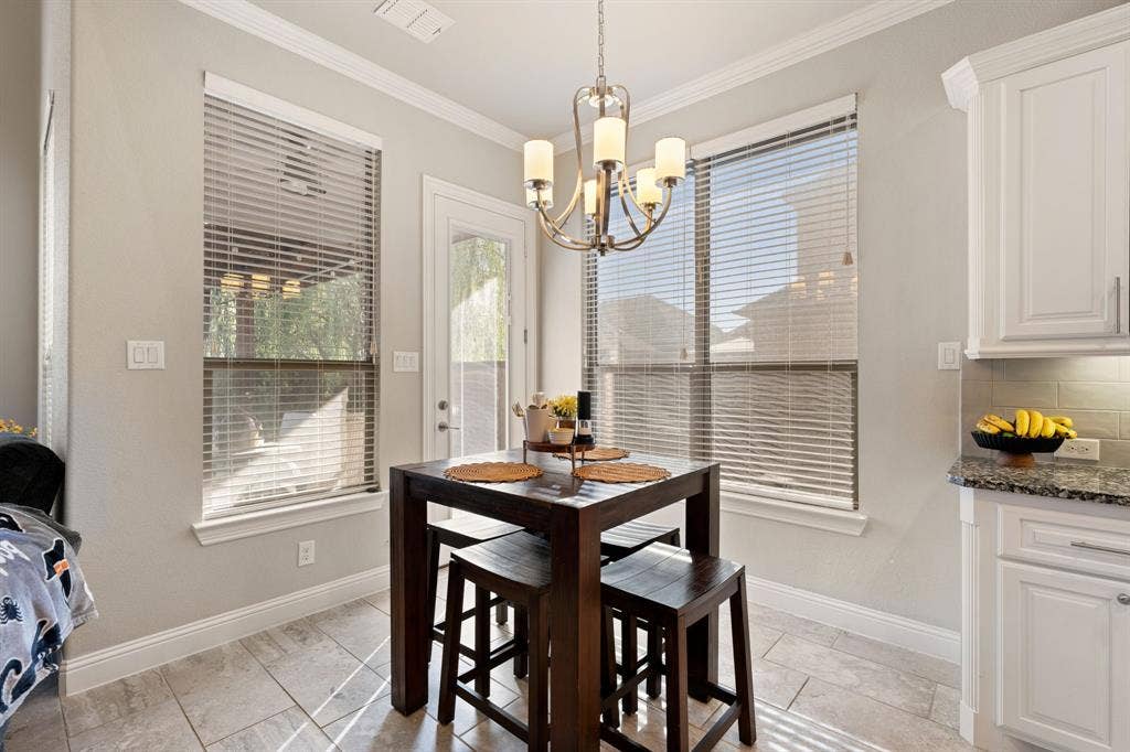 Tile flooring throughout, with a decorative chandelier, white cabinetry, granite countertops, and a subway tile backsplash