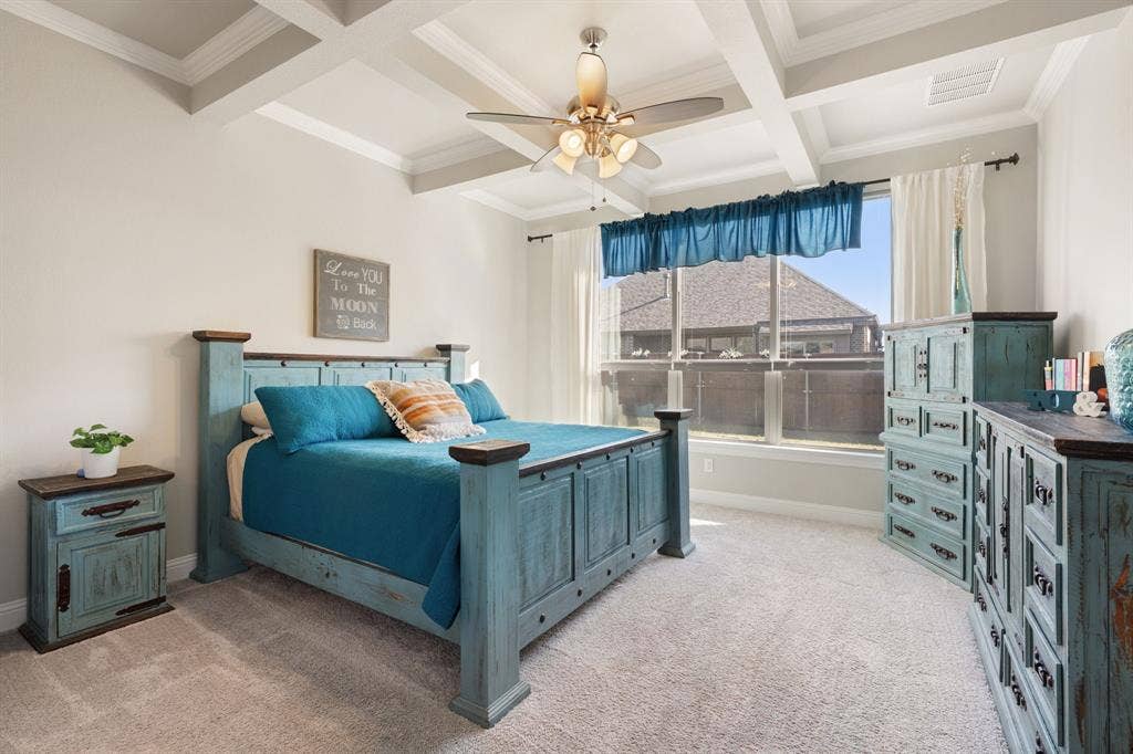 Coffered ceiling with a ceiling fan, broad window, and light-toned carpeting