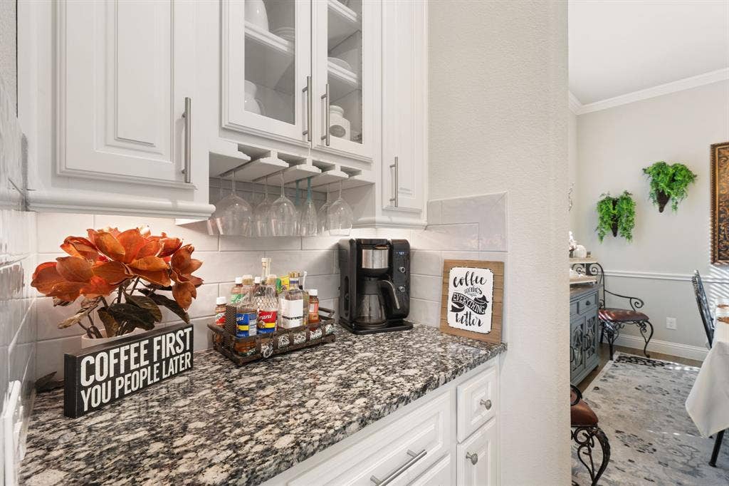 White shaker-style cabinetry with glass-front uppers, a built-in wine glass rack, granular countertop, and a white subway tile backsplash