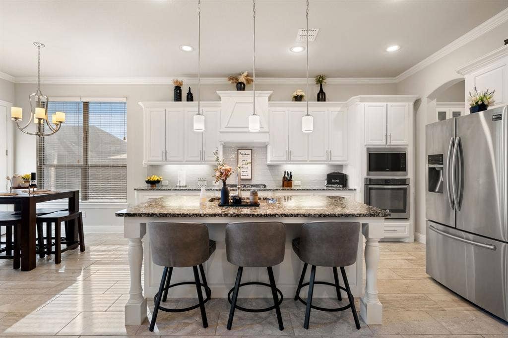 Spacious kitchen featuring an expansive center island with seating, white cabinetry, built-in stainless steel appliances, and tiled flooring
