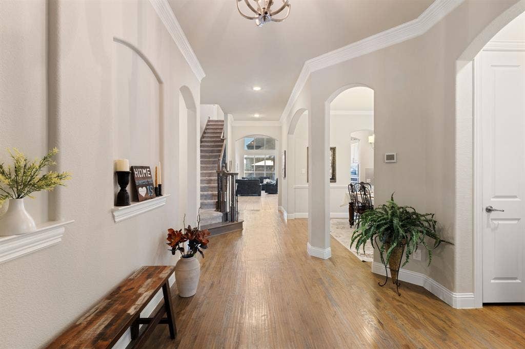 Expansive hallway with wood-finish flooring, arched doorways, crown molding, and a staircase with carpeted treads and dark wood banister