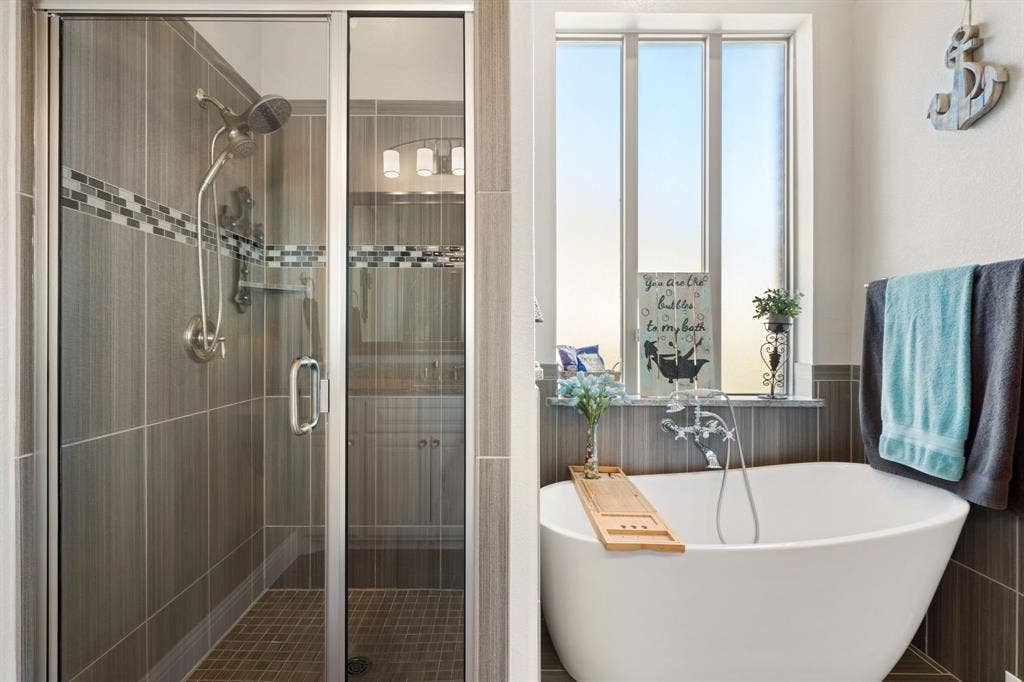 Freestanding soaking tub, walk-in shower with glass enclosure, mosaic tile accent, and floor-to-ceiling window