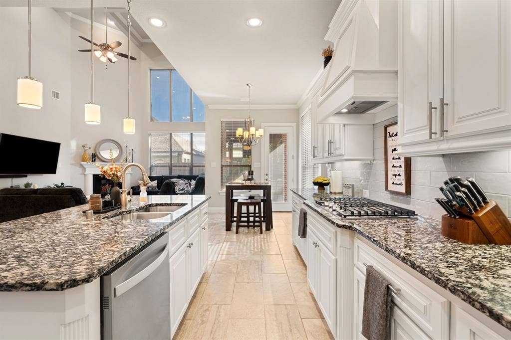 Kitchen island with integrated sink and stainless steel dishwasher, white cabinetry, gas cooktop with range hood, and tile flooring