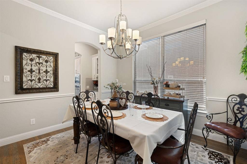 Wood-finish flooring, crown molding, chair rail molding, arched doorway, and chandelier lighting