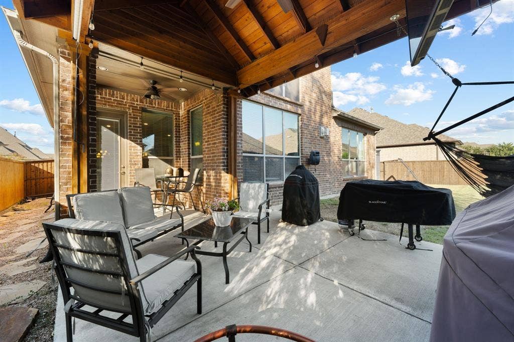 Expansive covered patio with wood beam ceiling and integrated shade structure, featuring a concrete floor and large sliding glass doors opening to the residence