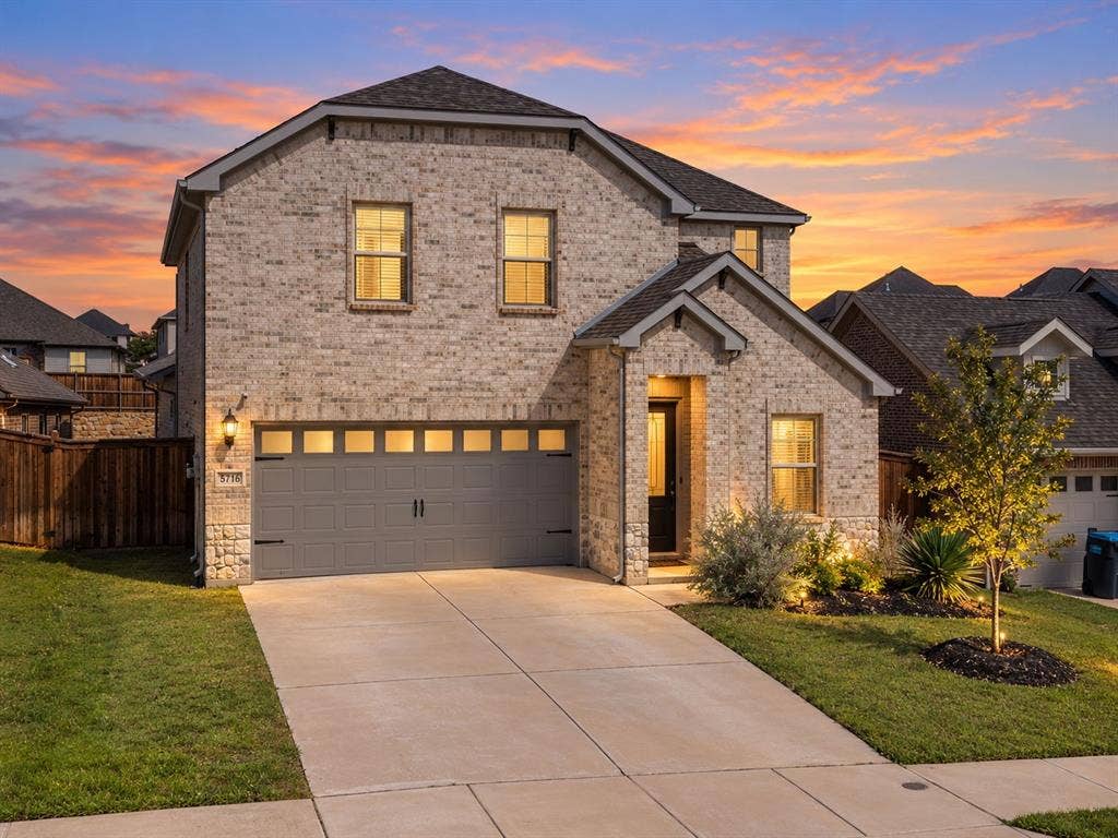 Brick exterior with stone accents, attached two-car garage, concrete driveway, and front yard landscaping