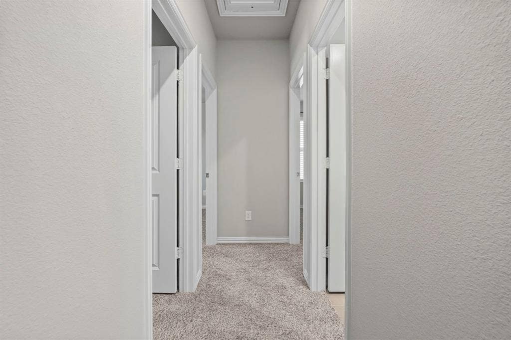 Hallway with light gray textured walls, white trim, and light gray carpeted flooring