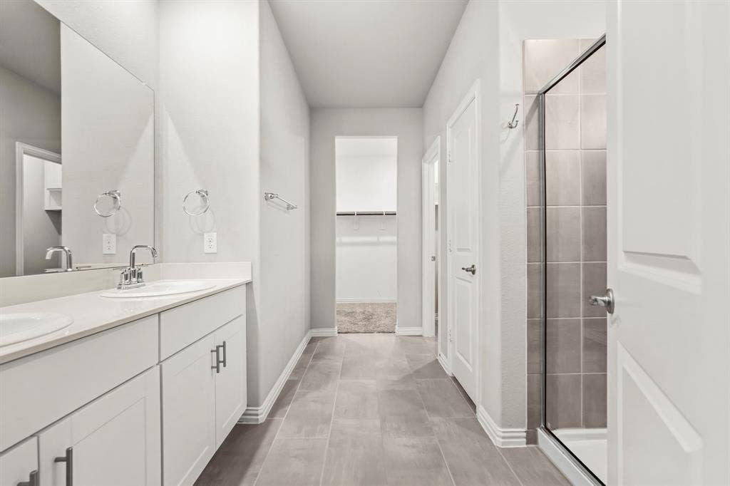 Dual vanity with white cabinetry and chrome fixtures, light-toned flooring, and a glass-enclosed shower with tiled walls