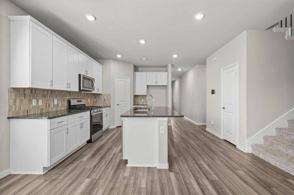Kitchen featuring white cabinetry, dark countertops, stainless steel appliances, and a hexagonal tile backsplash
