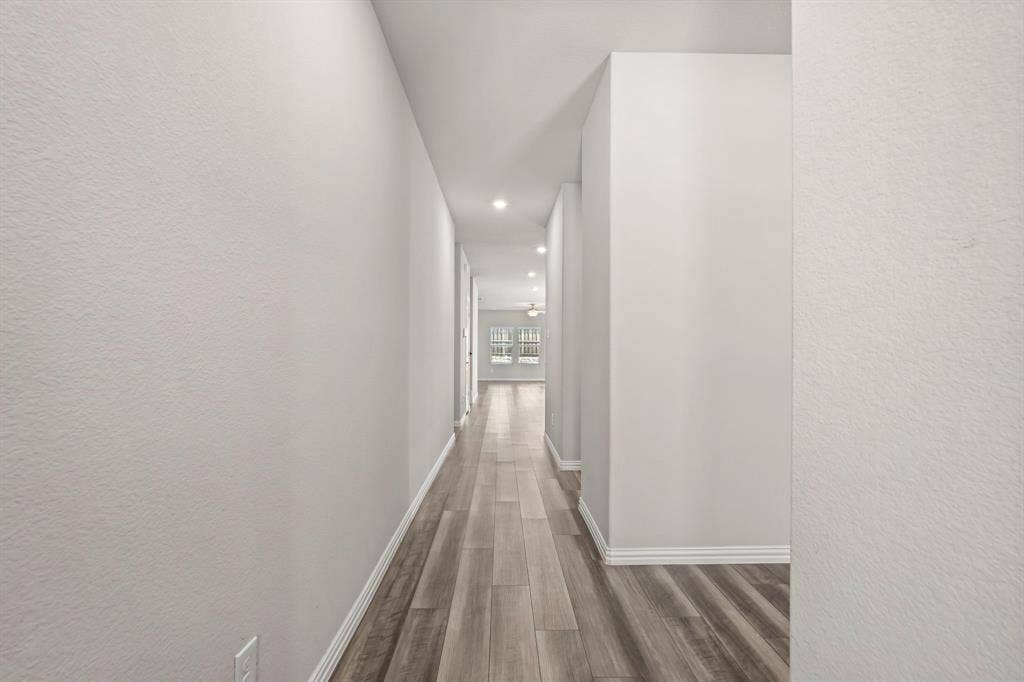 Recessed lighting illuminating a long hallway with wood-finish flooring and light-toned walls