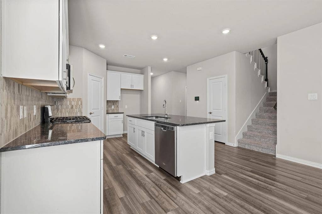 Open-concept kitchen with white cabinetry, dark granite countertops, and a full-height tiled backsplash