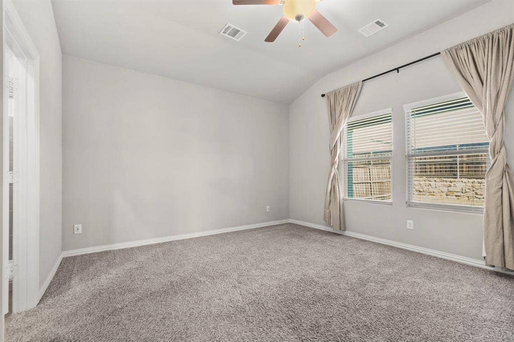 Vaulted ceiling, two windows with blinds, ceiling fan with light, light grey carpeting, and white baseboards