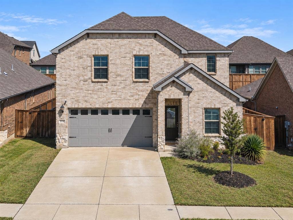 Brick exterior with stone accents, attached two-car garage, concrete driveway, front entry door, and landscaped front yard