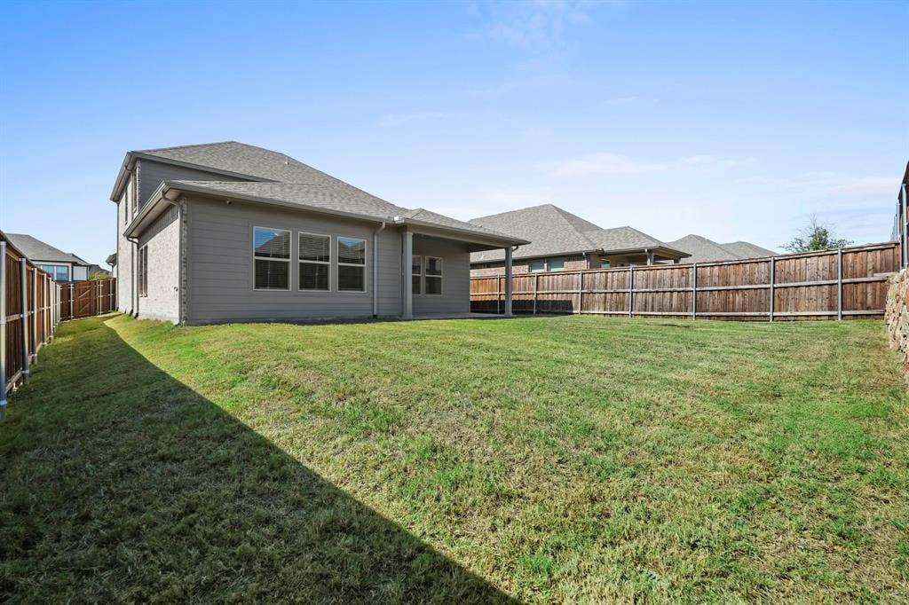 Expansive backyard with a flat lawn, wood-panel fencing, and a covered patio area