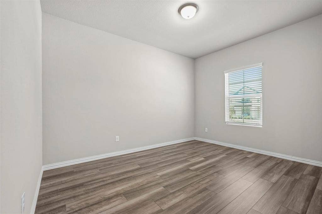 Wood-finish flooring, neutral wall tones, window with horizontal blinds, and a flush-mount ceiling light