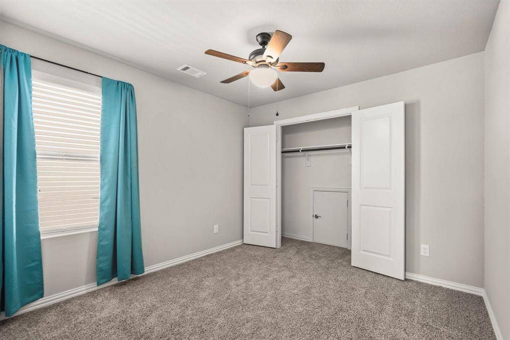 Carpeted flooring, a window with horizontal blinds, a ceiling fan with integrated lighting, and a bi-fold door closet with built-in shelving