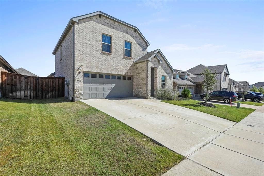 Brick exterior with a two-car garage, concrete driveway, and a wood privacy fence