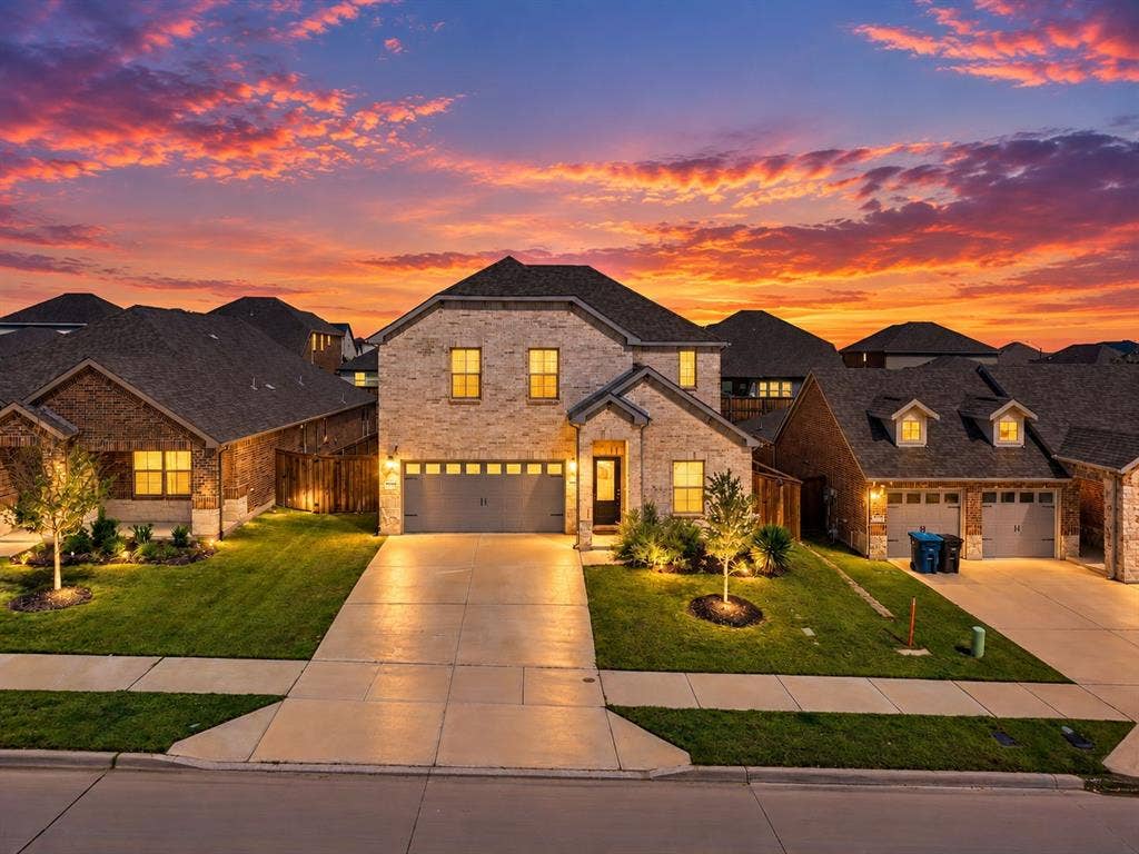 Stunning two-story residence showcasing a brick and stone exterior, arched roofline, and professional landscape lighting