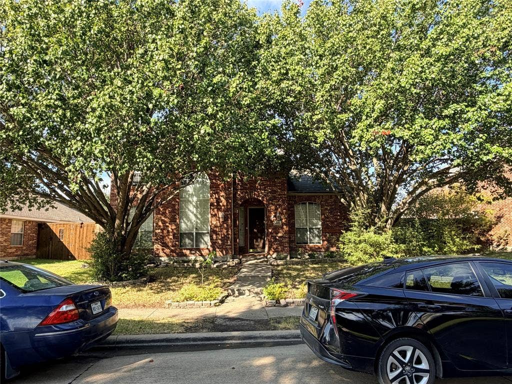 Charming brick residence nestled beneath mature, leafy trees providing natural shade and curb appeal