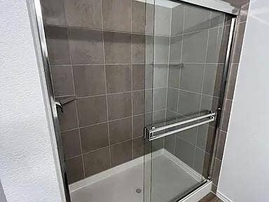 610 Grenada Lake Drive, Princeton, TX 75407 Modern shower enclosure featuring frameless glass sliding doors, chrome hardware, and subway tile walls in neutral tones