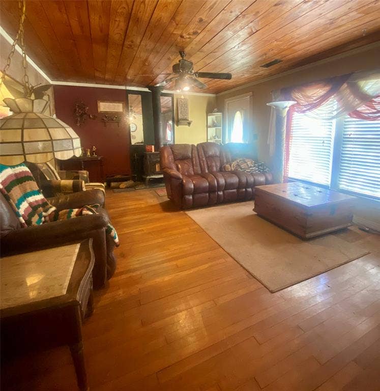 Spacious living area featuring warm wood-finish flooring throughout, wood plank ceiling with ceiling fan, and abundant natural light from multiple windows with plantation shutters