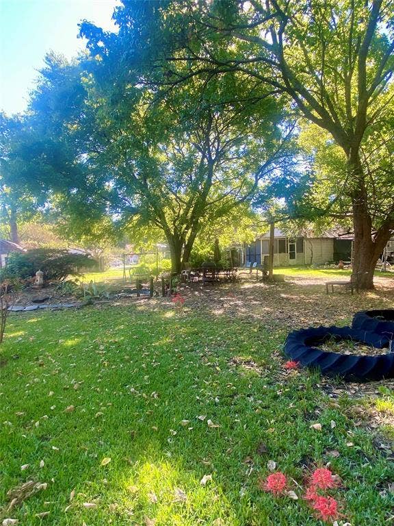 Expansive backyard featuring mature trees, a manicured lawn, and vibrant red flowering plants