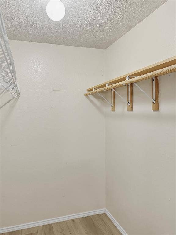 Spacious walk-in closet featuring natural wood-finish shelving and hanging rod system, recessed ceiling lighting, and wood-finish flooring throughout