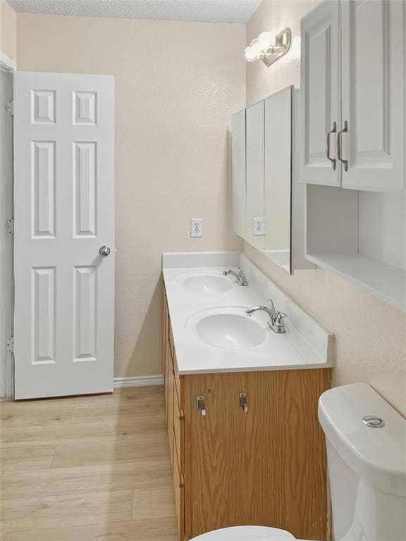 Dual vanity with integrated sinks, wood-finish cabinetry, white countertops, and wood-finish flooring