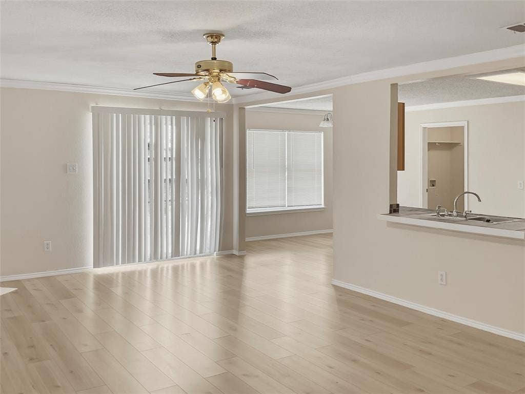 Wood-finish flooring throughout, sliding glass door with vertical blinds, ceiling fan with integrated lighting, breakfast bar with double basin sink, and crown molding accents
