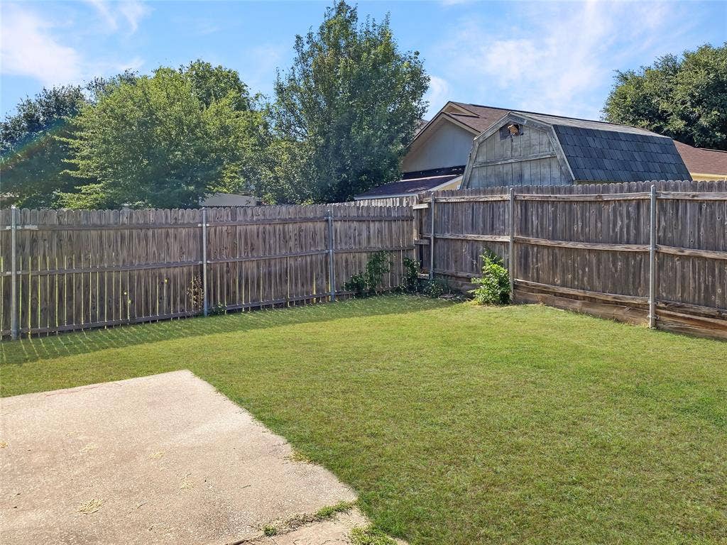 Spacious backyard oasis featuring a manicured lawn, concrete patio, and mature tree-lined perimeter enclosed by wood-finish fencing