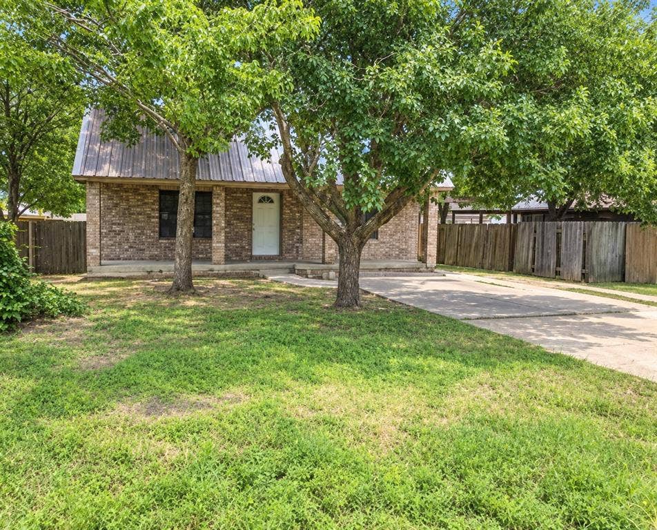 1017 W 3rd Street, Taylor, TX 76574 Front exterior view featuring a shaded lawn, mature trees, and a long private driveway.