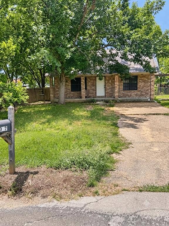 1017 W 3rd Street, Taylor, TX 76574 Street-level view of the front yard, highlighting mature shade trees and the paved driveway approach.