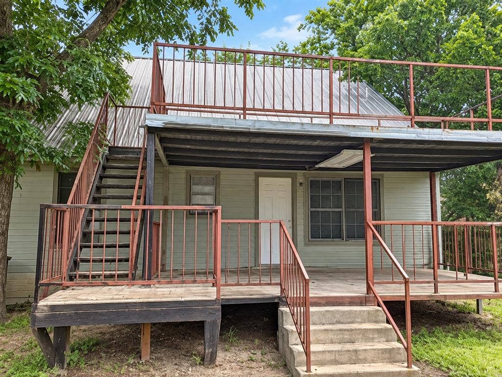 1017 W 3rd Street, Taylor, TX 76574 Rear exterior view showing the spacious back deck, wooden stairs, and second-story balcony access.