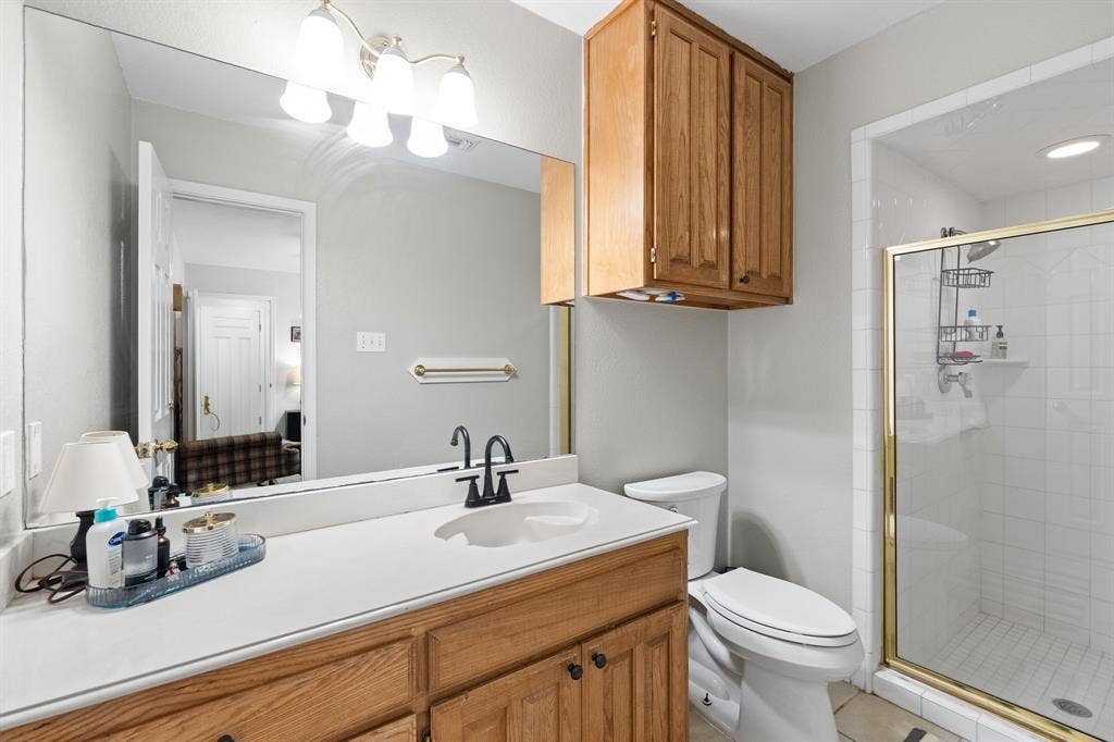 Vanity with a single basin and black-finish faucet, full-width mirror, light wood-finish cabinetry, built-in wall cabinet, and a glass-enclosed shower