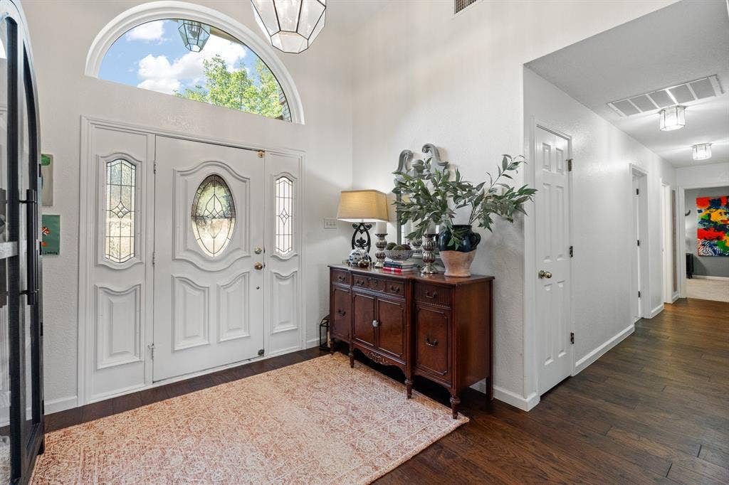 Entryway featuring a decorative front door with leaded glass panels, an arched transom window, and dark wood flooring