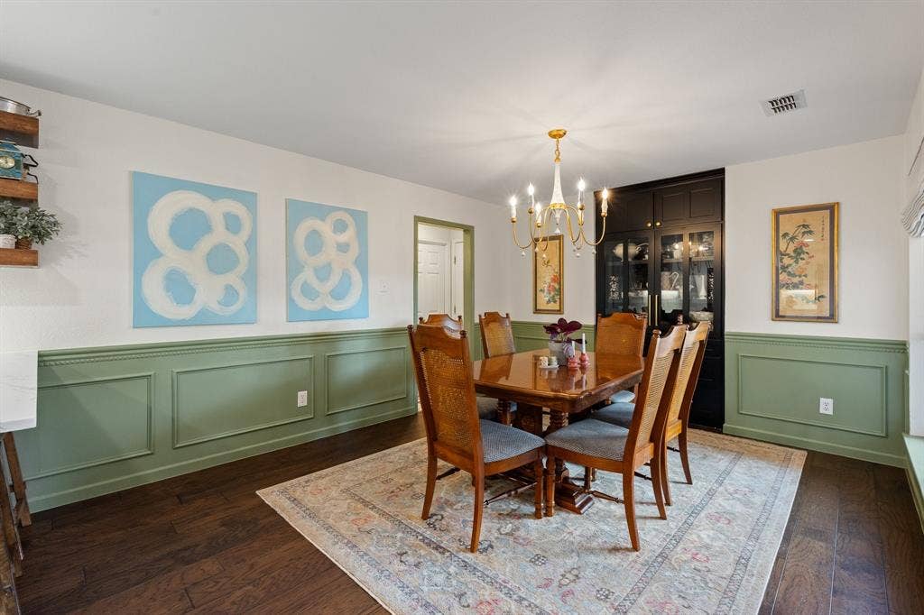Wood flooring, accent wainscoting, built-in cabinetry with glass paneling, and an overhead chandelier with candle-style lights