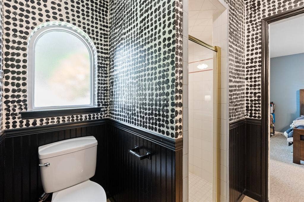 Arched window with privacy glass, black beadboard wainscoting, white toilet, and enclosed shower