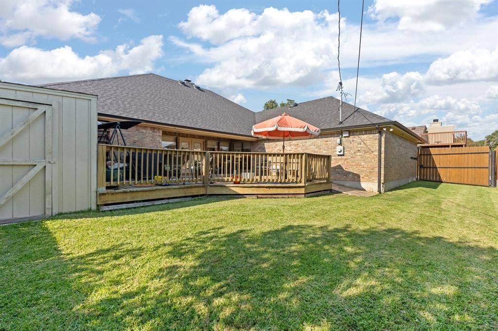 Expansive green lawn featuring a wooden deck, a brick exterior, a shed, and a privacy fence