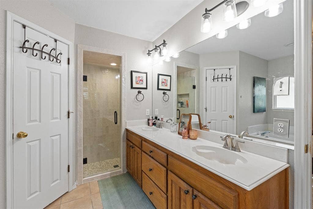 Double vanity with integrated sinks, wood-finish cabinetry, new frameless glass shower enclosure, and tiled shower interior