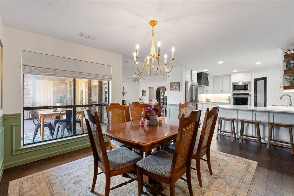 Wood flooring, a gold-tone chandelier, and a large window with a Roman shade