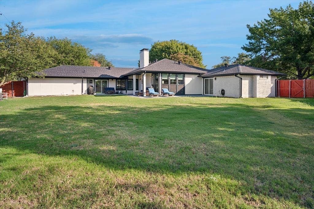 10102 Laingtree Drive, Dallas, TX 75243 Expansive backyard featuring a manicured lawn, masonry chimney, covered patio, and perimeter wood fencing