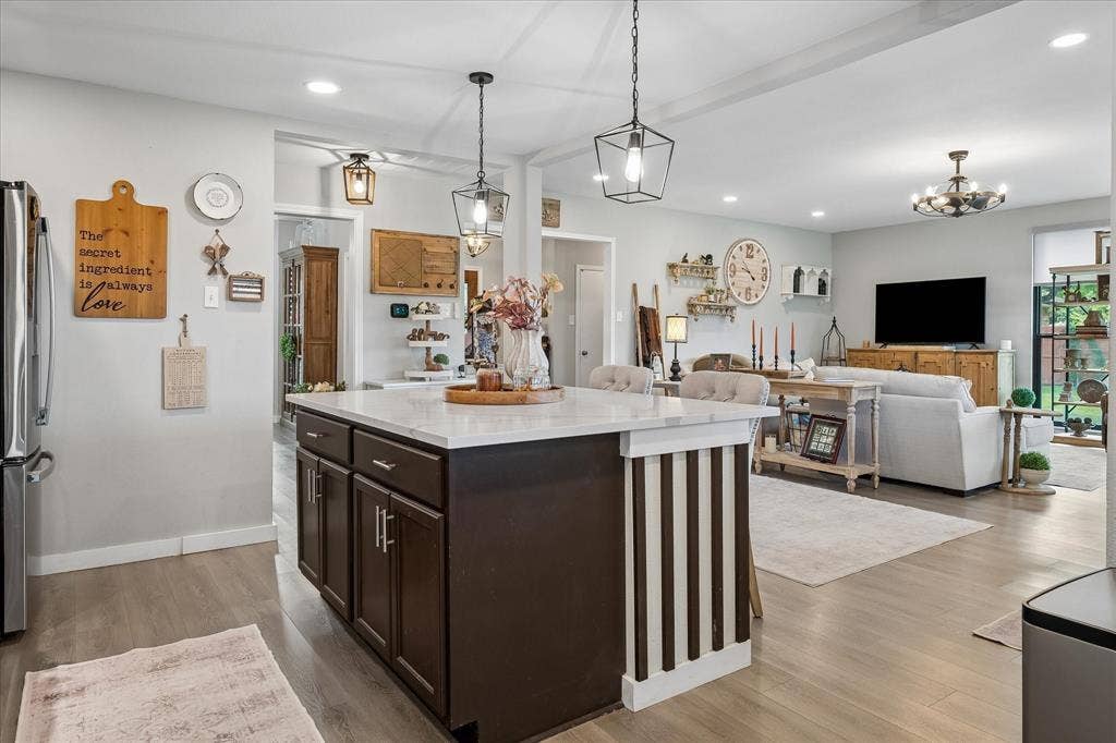 10102 Laingtree Drive, Dallas, TX 75243 Kitchen island with stone-surface countertop, dark-finish cabinetry, wood-finish flooring, and industrial-style pendant lighting