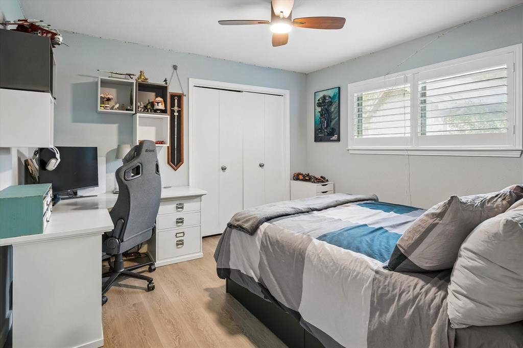 10102 Laingtree Drive, Dallas, TX 75243 Light-filled room featuring wood-finish flooring, a ceiling fan with integrated lighting, dual-panel closet doors, and plantation shutters