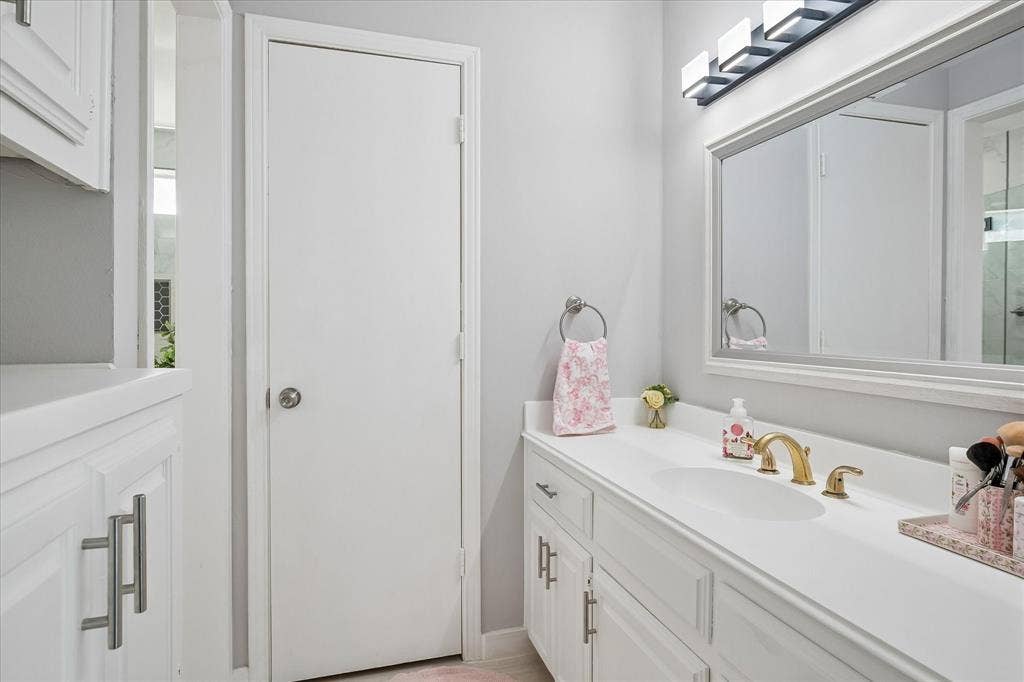 10102 Laingtree Drive, Dallas, TX 75243 Bathroom vanity with white cabinetry, solid surface countertop, integrated sink, brass finish faucet, and rectangular wall-mounted mirror
