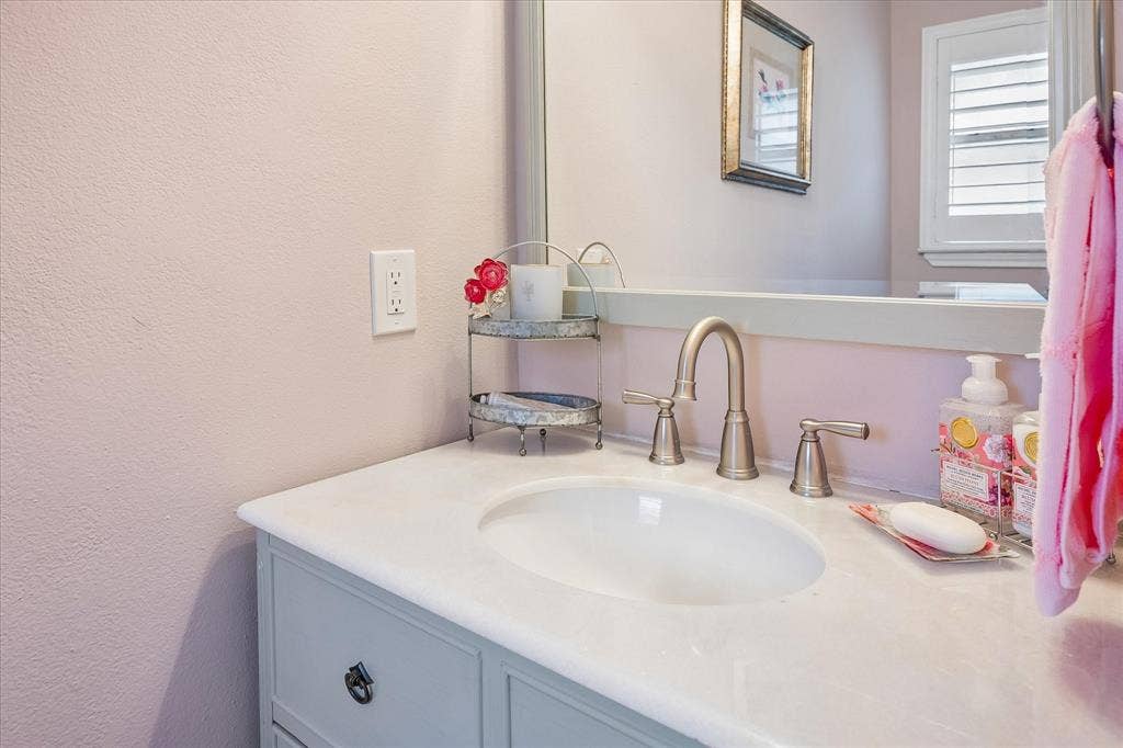 10102 Laingtree Drive, Dallas, TX 75243 Bathroom vanity featuring a light-toned countertop with an integrated oval sink, brushed metal widespread faucet, neutral-toned cabinetry, and a large wall-mounted mirror