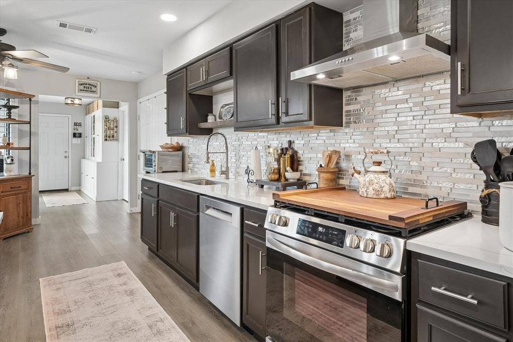 10102 Laingtree Drive, Dallas, TX 75243 Kitchen featuring dark cabinetry, solid-surface countertops, horizontal glass-tile backsplash, stainless steel appliances, and wood-finish flooring