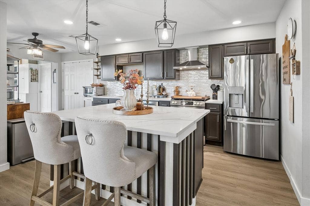 10102 Laingtree Drive, Dallas, TX 75243 Kitchen featuring dark wood cabinetry, a central island with a white stone-surface countertop, stainless steel appliances, a tile backsplash, and wood-finish flooring