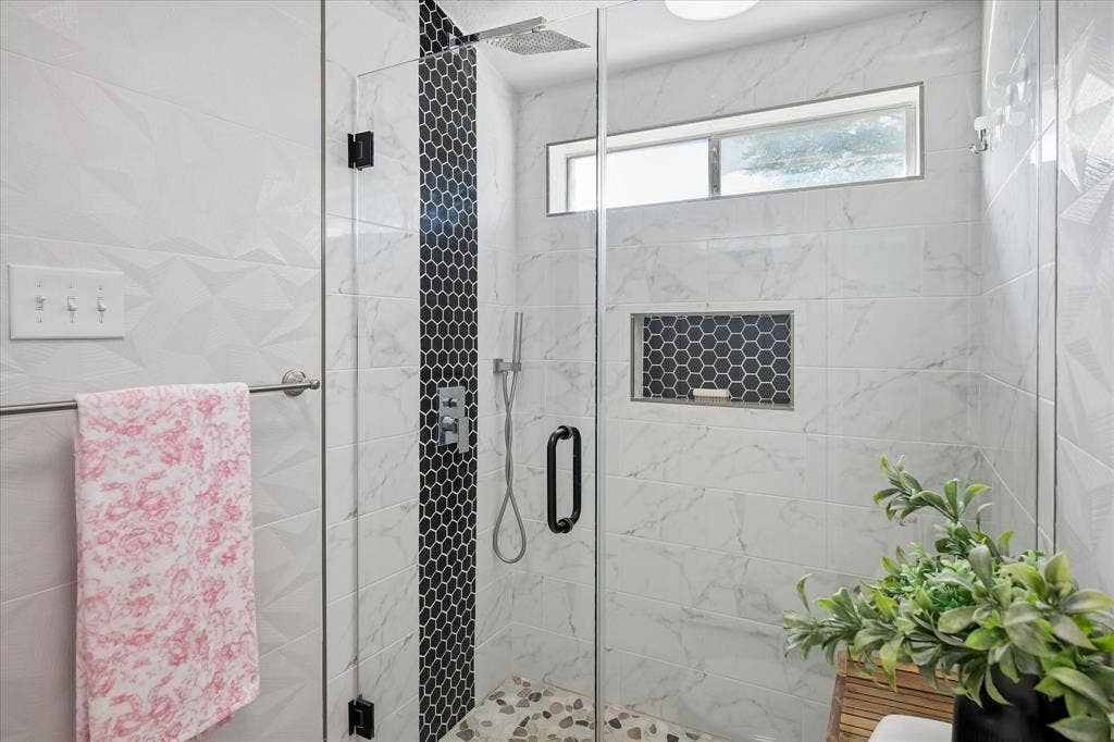 10102 Laingtree Drive, Dallas, TX 75243 Walk-in shower featuring large-format white tile walls with textured geometric patterns, black hexagonal accent tiling, a built-in recessed niche, rainfall showerhead, and a clear glass enclosure